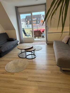 En moderne stue med sofa, rundt sofabord og balkon med udsigt til bygninger.