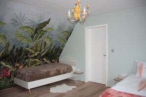A bedroom with a bed, a chandelier, a door, and a wall with a plant mural.