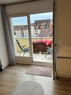 Et værelse med en skydedør til en udendørs balkon med bord og stole, en radiator og trægulv.