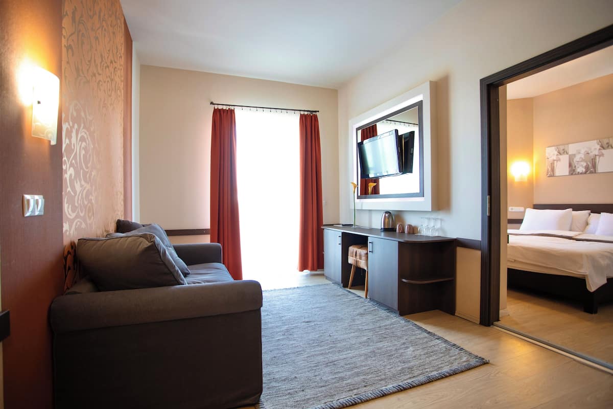A hotel room with a sofa, a desk, a bed, a TV, and a large window with curtains.