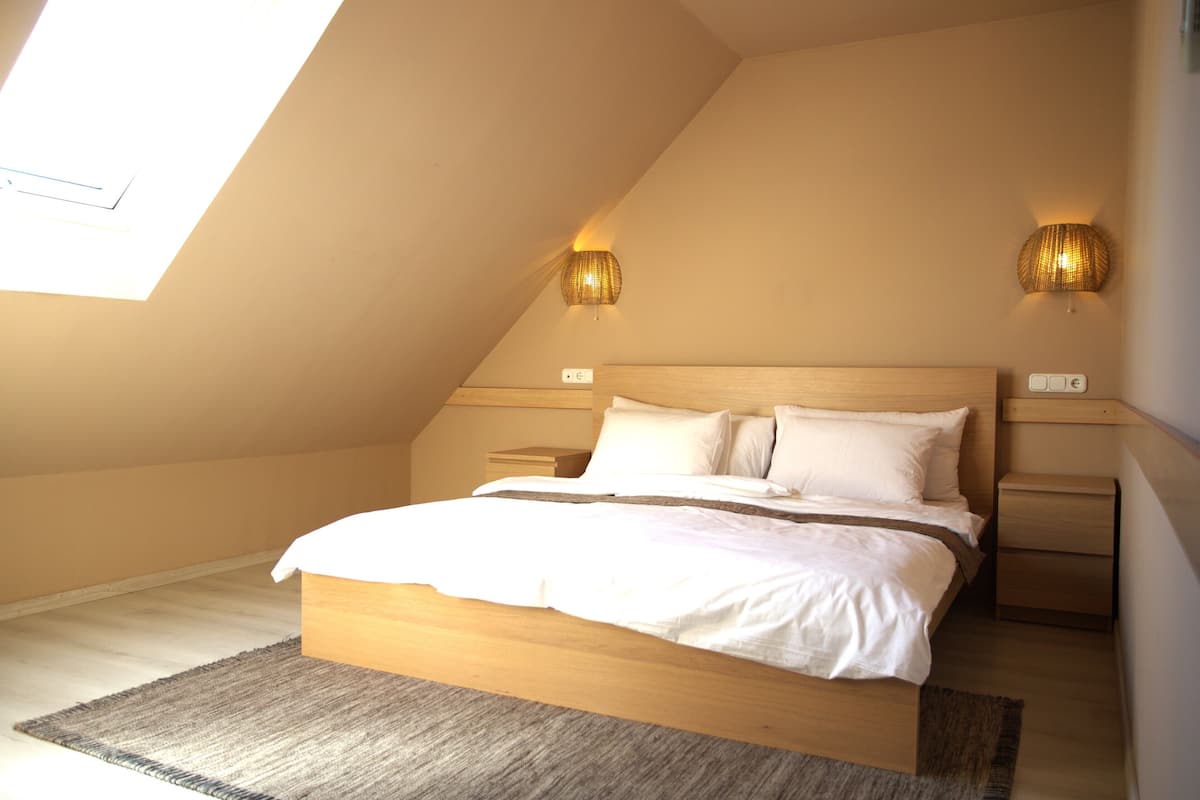 A bedroom with a sloped ceiling, a wooden bed, two bedside lamps, and a small nightstand.