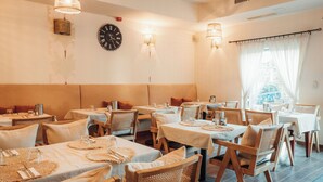 Un restaurant avec des tables dressées pour le service, des chaises en osier et une horloge au mur.