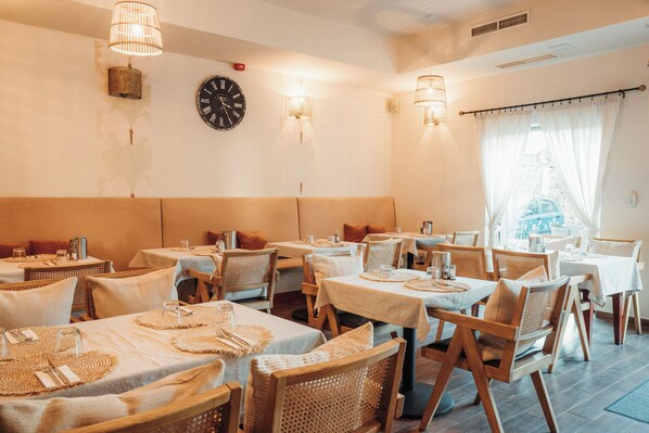 Un restaurant avec des tables dressées pour le service, des chaises en osier et une horloge au mur.