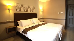 Une chambre d’hôtel avec un grand lit, deux tables de chevet, des lampes fixées au mur et une œuvre d’art florale au-dessus du lit.