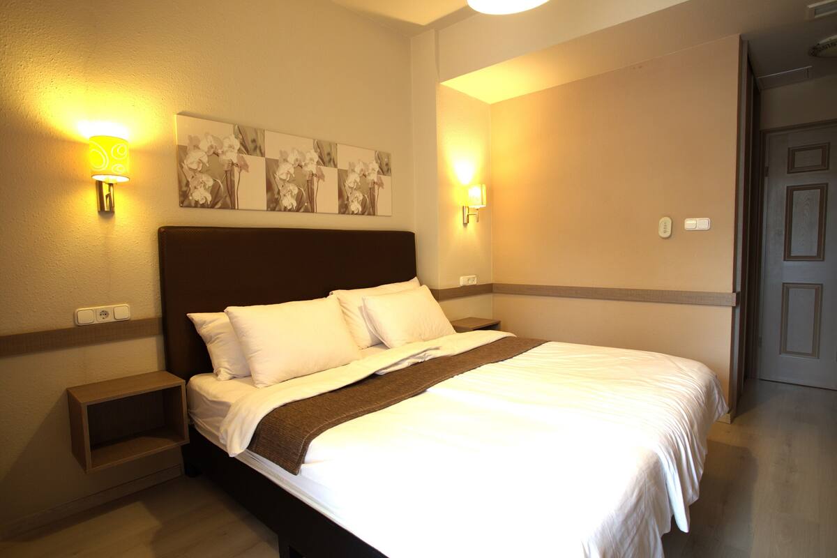 A hotel room with a large bed, two bedside tables, wall-mounted lamps, and a floral artwork above the bed.