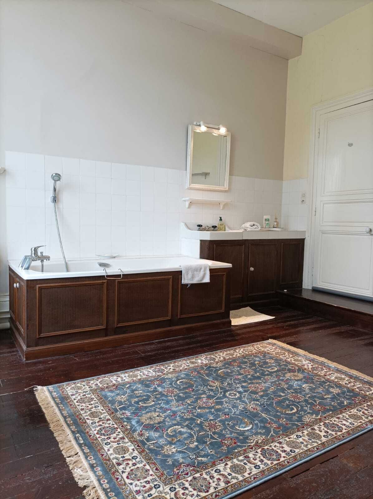 Un baño con una bañera independiente, un espejo grande y un tapete estampado en el suelo.