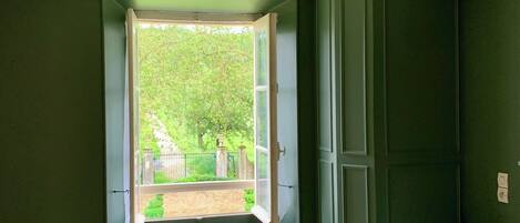 A bathroom with a green wall, a white toilet, and a window with a view of greenery outside.