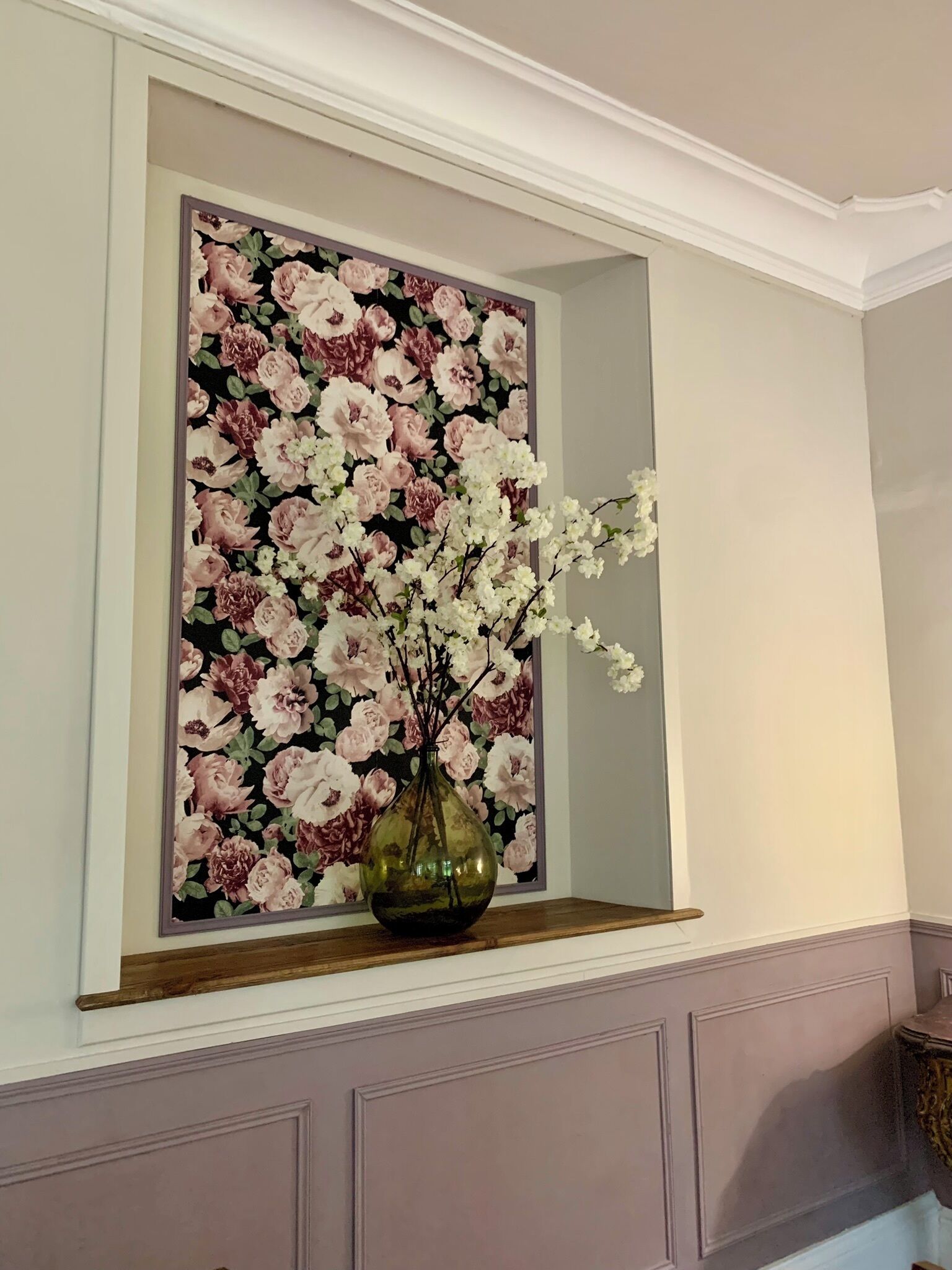 Una obra de arte floral enmarco sobre una pared, encima de un estante de madera.
