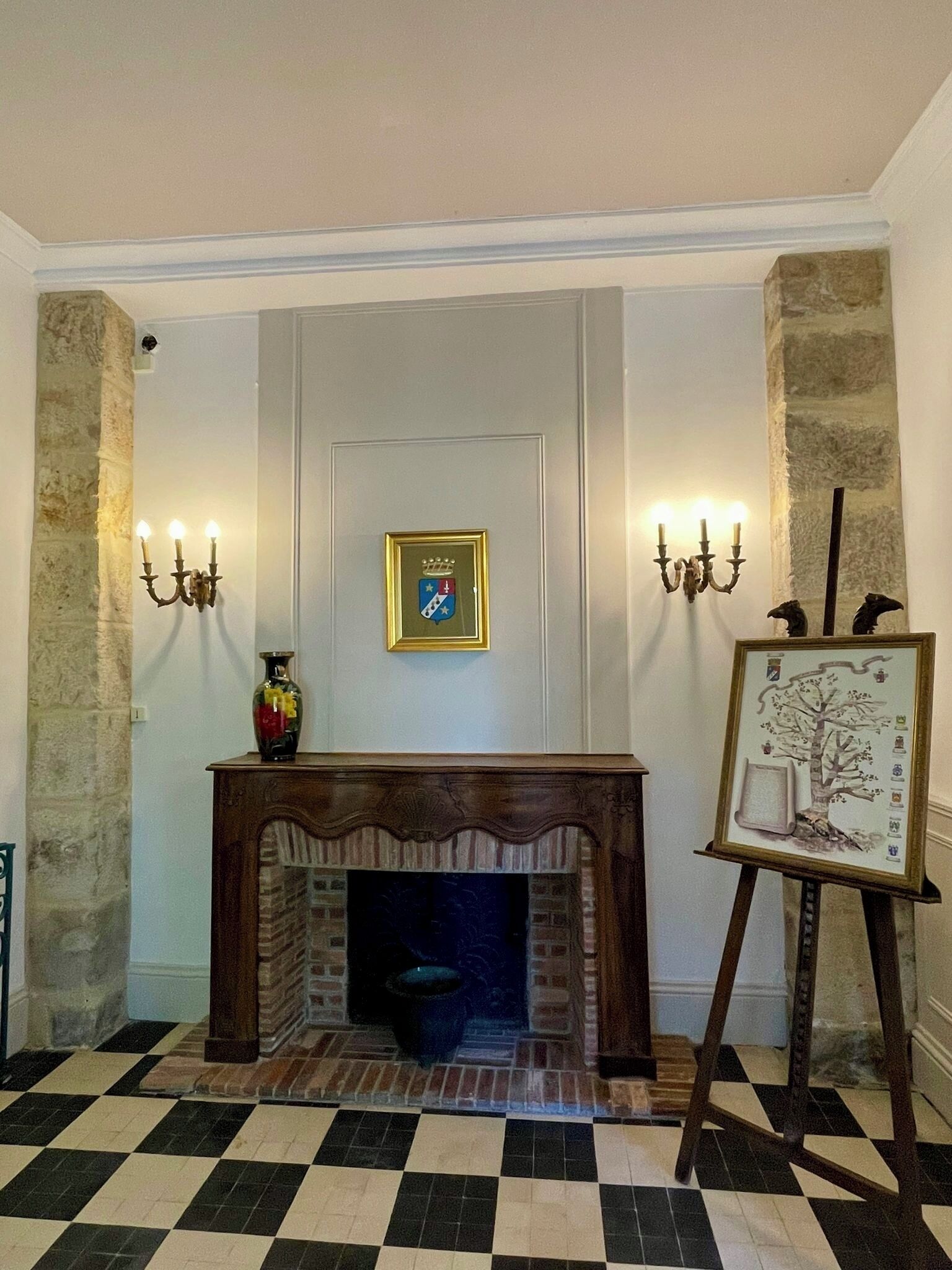 Una habitación con chimenea, un escudo enmarcados en la pared y una pintura sobre caballete.
