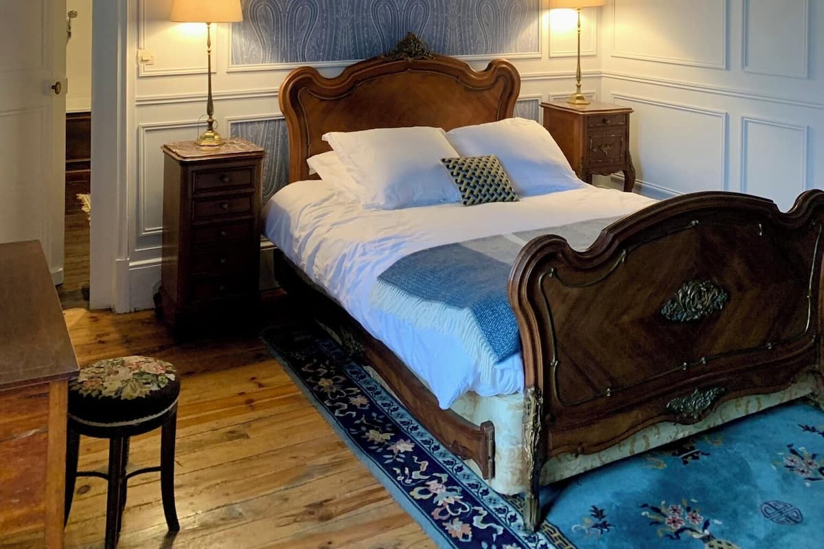 A bedroom with a wooden bed, two bedside tables, a patterned wall, and a wooden floor.