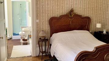 Een slaapkamer met een houten bed, een nachtkastje, een lamp en een zichtbare badkamer door een geopende deur.