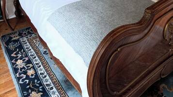 Un lit avec une tête de lit en bois, une literie blanche, un coussin décoratif, une couverture grise et un tapis à motifs.