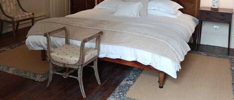 A bedroom with a wooden bed, two bedside tables with lamps, a chair, and a hanging light fixture.