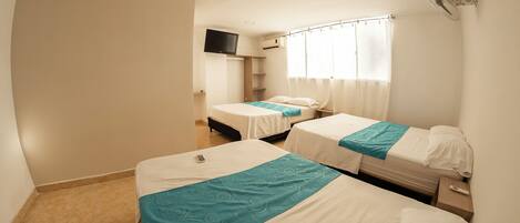 Habitación de hotel con dos camas individuales, un televisor montado en la pared y una ventana con cortinas.