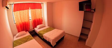 A small, compact room with two single beds, a window with red curtains, a ceiling fan, and a small staircase.
