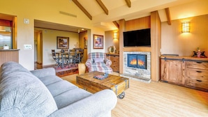 A cozy living room with a fireplace, a sofa, a coffee table, and a television. - Suncadia Penthouse with Mountain Views, Full Kitchen and Pool Hot Tub Access (Cle Elum)