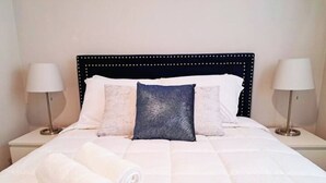 Ein ordentlich bezogenes Bett mit weißen Leinen, einem zusammengerollten Handtuch und einem dunkelblauen Kopfkissen.