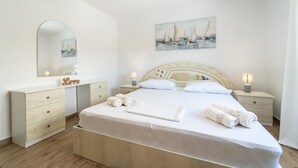 A bedroom with a bed, bedside tables, a dresser, a mirror, and a painting of sailboats.