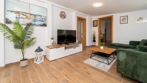 A modern living room with a flat-screen TV, wooden coffee table, green sofa, and a large potted plant.