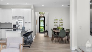 Una cocina moderna con armarios blancos, una isla central y un comedor con mesa y sillas de madera.