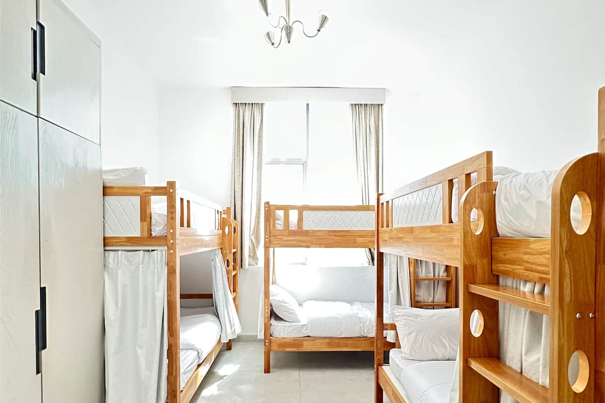 Une chambre d’hôtel avec trois lits superposés en bois, une armoire, un lustre et une grande fenêtre avec des rideaux.