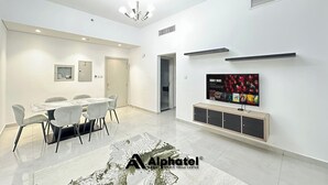 Un salon moderne comprenant un coin repas, un téléviseur fixé au mur et un lustre.