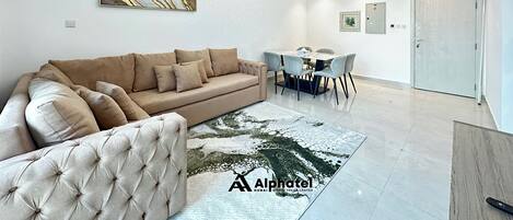 A modern living room with a sofa, a tufted armchair, a dining table with chairs, and a chandelier.