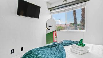 A bedroom with a bed, a window with a view, a mounted TV, and a green knitted blanket.