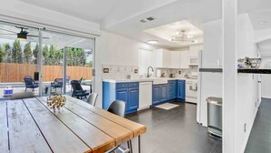 Una cocina moderna con armarios azules, una mesa de comedor de madera y vistas al jardín trasero a través de puertas de vidrio.