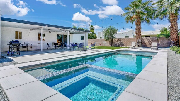 Una piscina con solárium de baldosas, mobiliario de exterior y palmeras.