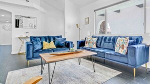 Una sala de estar moderna con un sofá azul, una mesa de centro de madera y un ventanal grande.