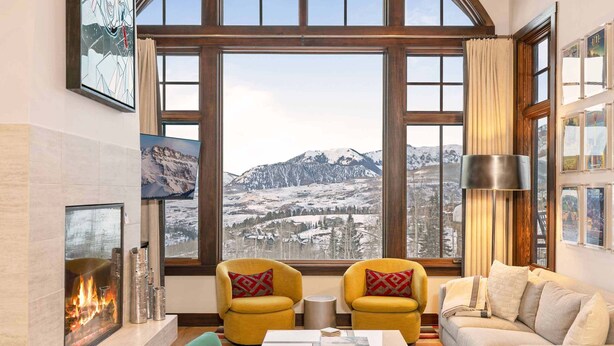 A cozy living room with a fireplace, two yellow armchairs, a green sofa, and a large window offering a mountain view. - Courcheval Chalet in Mt Village Core with use of 2 free ski passes during stay! (Mountain Village)