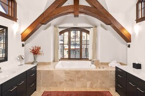 Une salle de bain moderne avec une grande baignoire, deux lavabos et une fenêtre avec des rideaux.