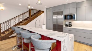 A modern kitchen with a marble countertop, stainless steel appliances, and a red accent wall. - Courcheval Chalet in Mt Village Core with use of 2 free ski passes during stay! (Mountain Village)