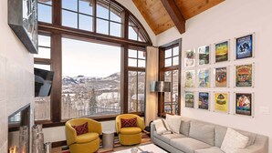 A living room with a fireplace, large windows, a sofa, a yellow armchair, and a coffee table. - Courcheval Chalet in Mt Village Core with use of 2 free ski passes during stay! (Mountain Village)