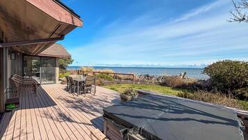Une terrasse en bois avec un jacuzzi, une table et des chaises, et une vue sur l’océan.