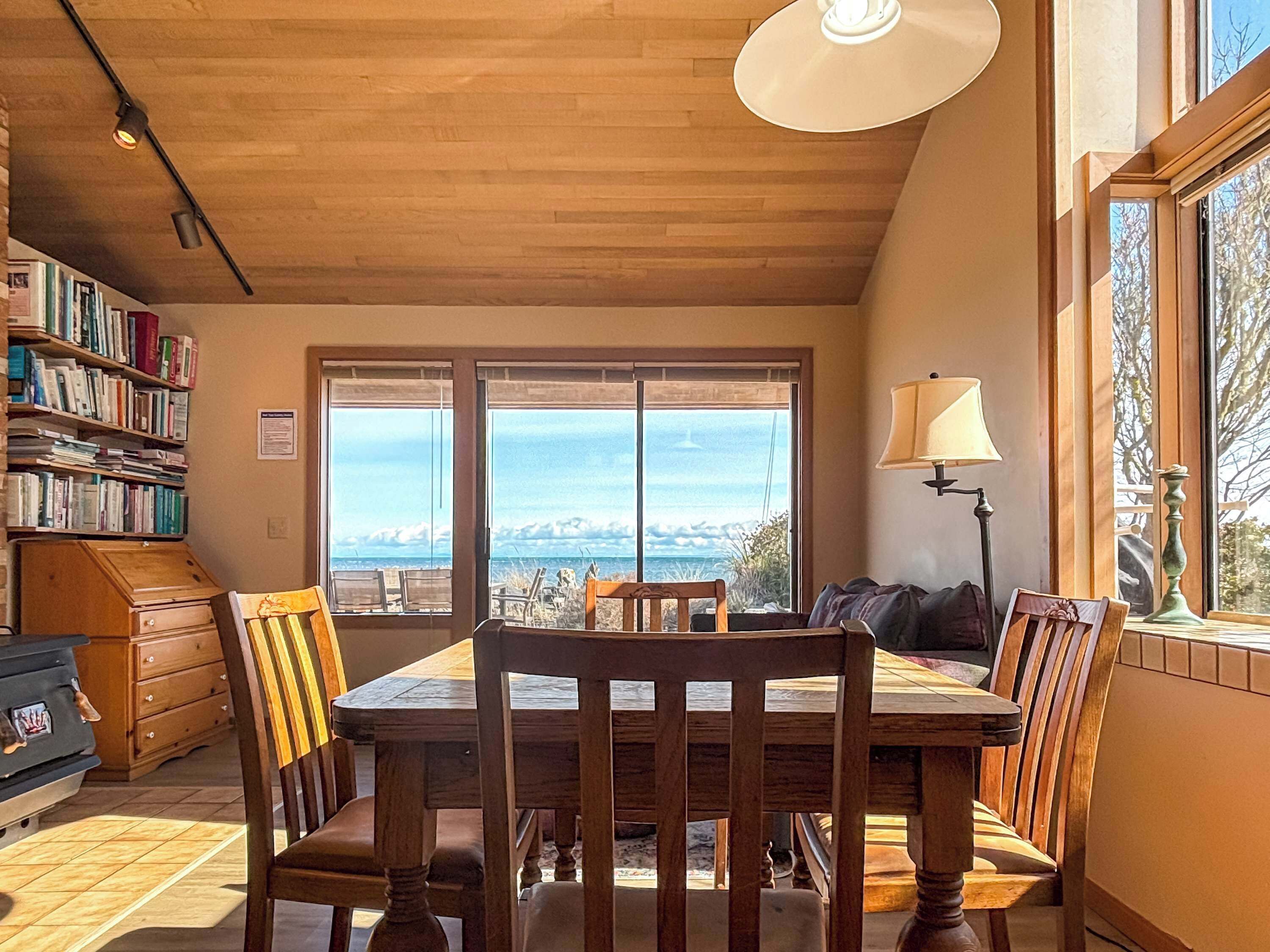 Un coin repas avec une table et des chaises en bois, une bibliothèque et une vue dégagée grâce à de grandes fenêtres.