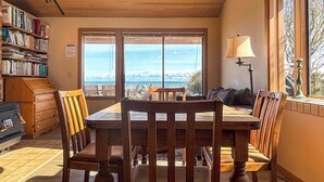 A dining area with a wooden table and chairs, a bookshelf, and a view through large windows. - Waterfront, Hot tub, Pets OK, Sequim Dungeness (Sequim)