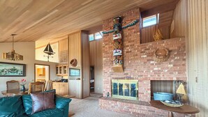 A cozy living room with a brick fireplace, wooden accents, and a green leather sofa. - Waterfront, Hot tub, Pets OK, Sequim Dungeness (Sequim)