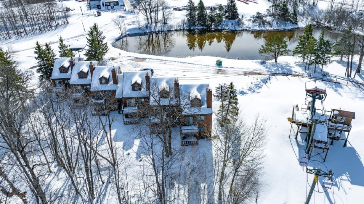 A snow-covered lodge with multiple cabins, a pond, and a ski lift.