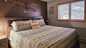 A bedroom with a large bed, a wooden headboard, a ski-themed wall hanging, and a window with blinds. - Ski in/Ski Out Entire Condo Sleeps 4 @ Jackson Creek Summit (Wakefield)