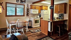 A kitchen with wooden cabinets, a dining table with chairs, and a built-in island with stools. - Ski in/Ski Out Entire Condo Sleeps 4 @ Jackson Creek Summit (Wakefield)