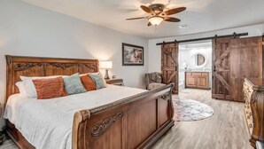 A bedroom with a wooden bed, a ceiling fan, and a view into the kitchen through a sliding barn door. - Charming 3-bedroom house in Shawnee with AC and WiFi (Shawnee)