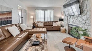 A modern living room with a brown leather sofa, a coffee table, and a stone fireplace. - Charming 3-bedroom house in Shawnee with AC and WiFi (Shawnee)