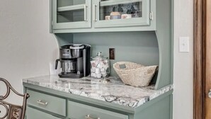 A kitchen with a marble countertop, a Keurig coffee maker, a basket, and a cabinet with glass doors containing jars and containers. - Charming 3-bedroom house in Shawnee with AC and WiFi (Shawnee)