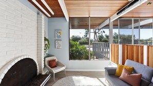 Una sala de estar moderna con chimenea, sofá, sillón y un ventanal con vistas a la vegetación.