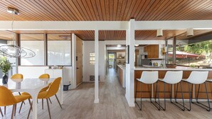 Una cocina moderna con armarios blancos, techo de madera y una barra con taburetes blancos.