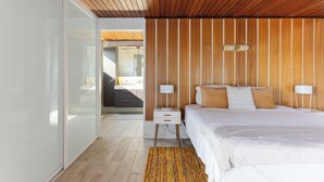 Un dormitorio moderno con techo de madera, una cama grande con ropa de cama blanca, dos mesitas de noche con lámparas y una alfombra colorida.