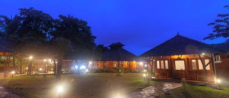 A series of thatched-roof buildings with illuminated windows and a paved pathway.