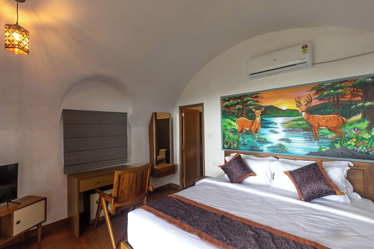 Et soveværelse med seng, skrivebord, stol, fjernsyn og et billede af dådyr.
